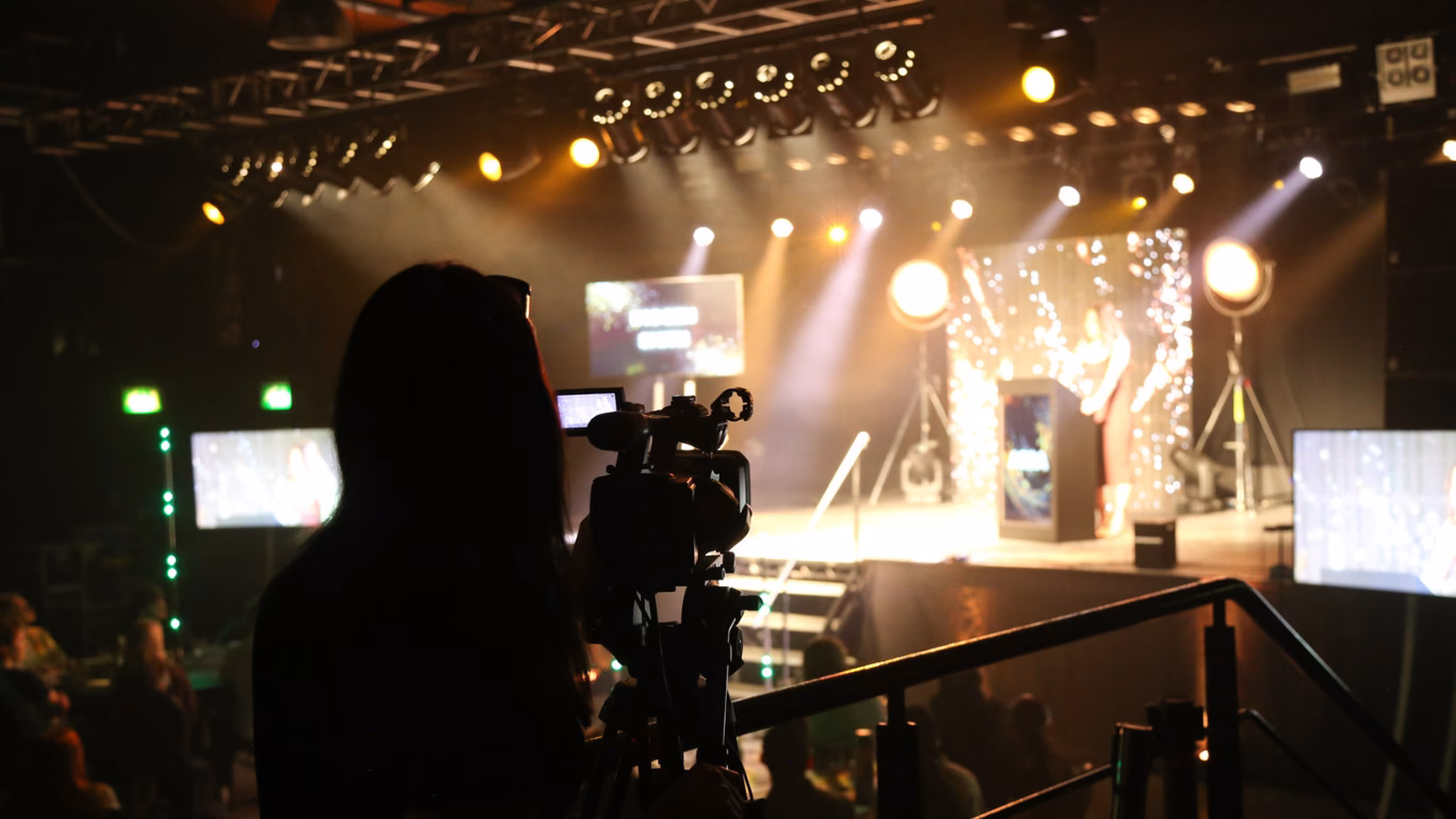 Videographer filming a live awards event with stage lights, presenter at podium, and audience in the background