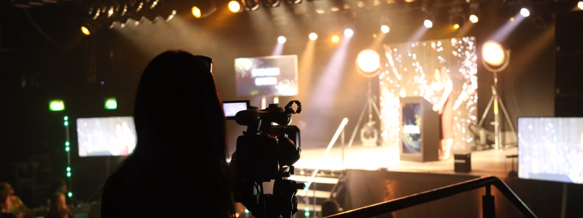 Videographer filming a live awards event with stage lights, presenter at podium, and audience in the background